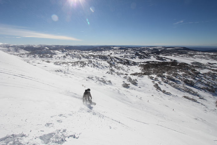 Snowboarder slashing boot deep snow on Olympic at Perisher