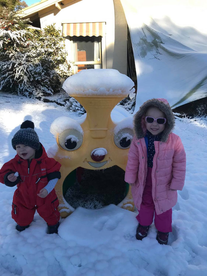 Happy kids enjoying the snow their dad made them in Canberra backyard